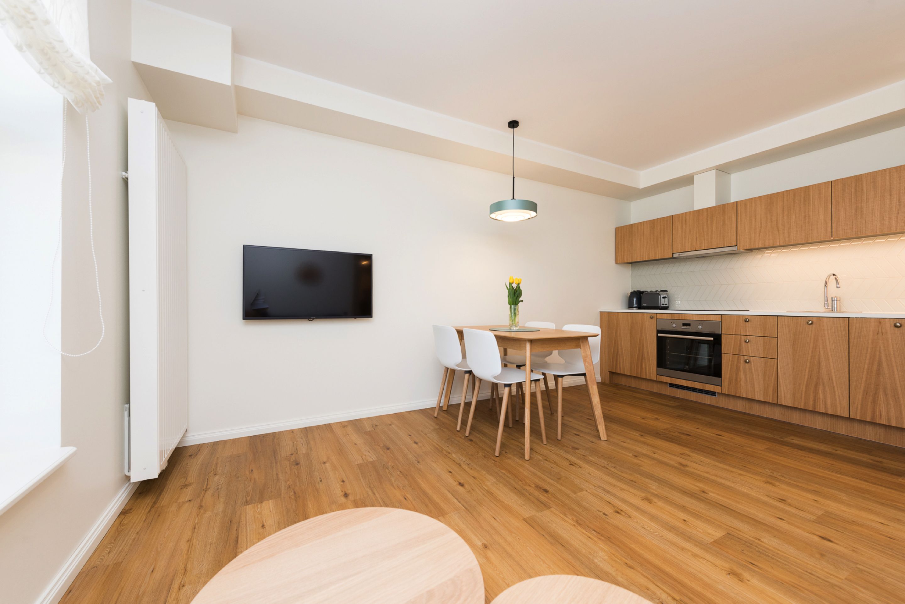 Une cuisine moderne avec des meubles en bois, un four encastré et un coin repas comprenant une table et des chaises.