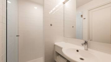 A modern bathroom with white tiles, a glass shower enclosure, a sink with a mirror, and a towel rack.