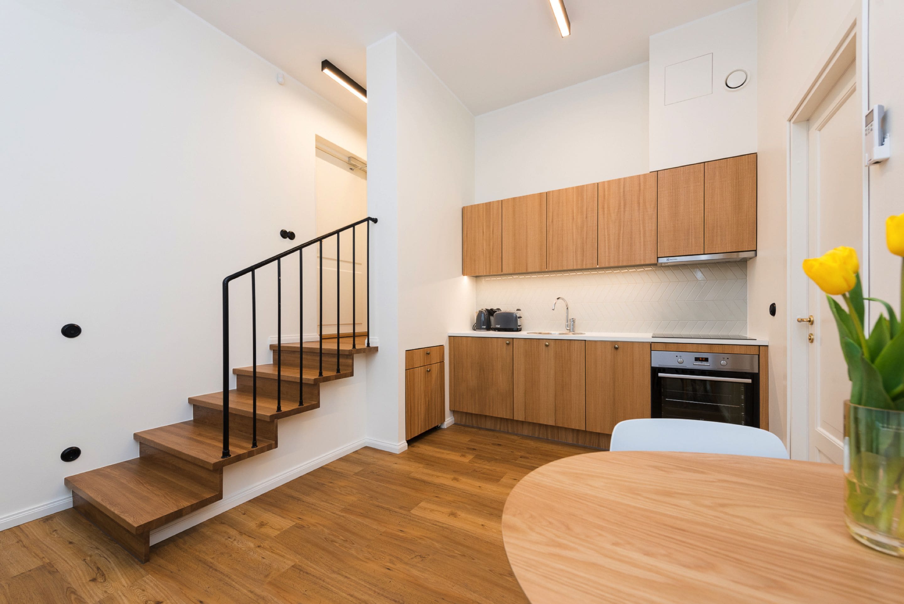 A modern kitchen with wooden cabinets, a built-in oven, and a dining area with a wooden table.