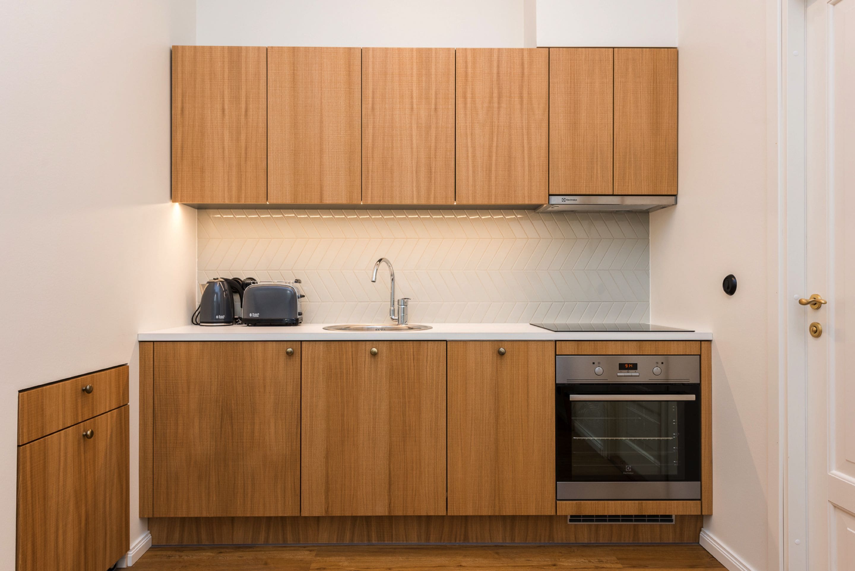 Cozinha compacta com armários de madeira, forno embutido e cafeteira.