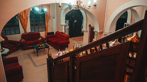 A spacious living area with red sofas, a coffee table, and a chandelier. There are arched doorways and a staircase leading to another level. - Hostal la Magia de Uyuni (Uyuni)