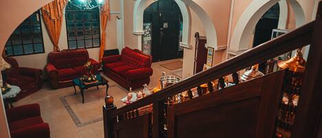 A spacious living area with red sofas, a coffee table, and a chandelier. There are arched doorways and a staircase leading to another level.