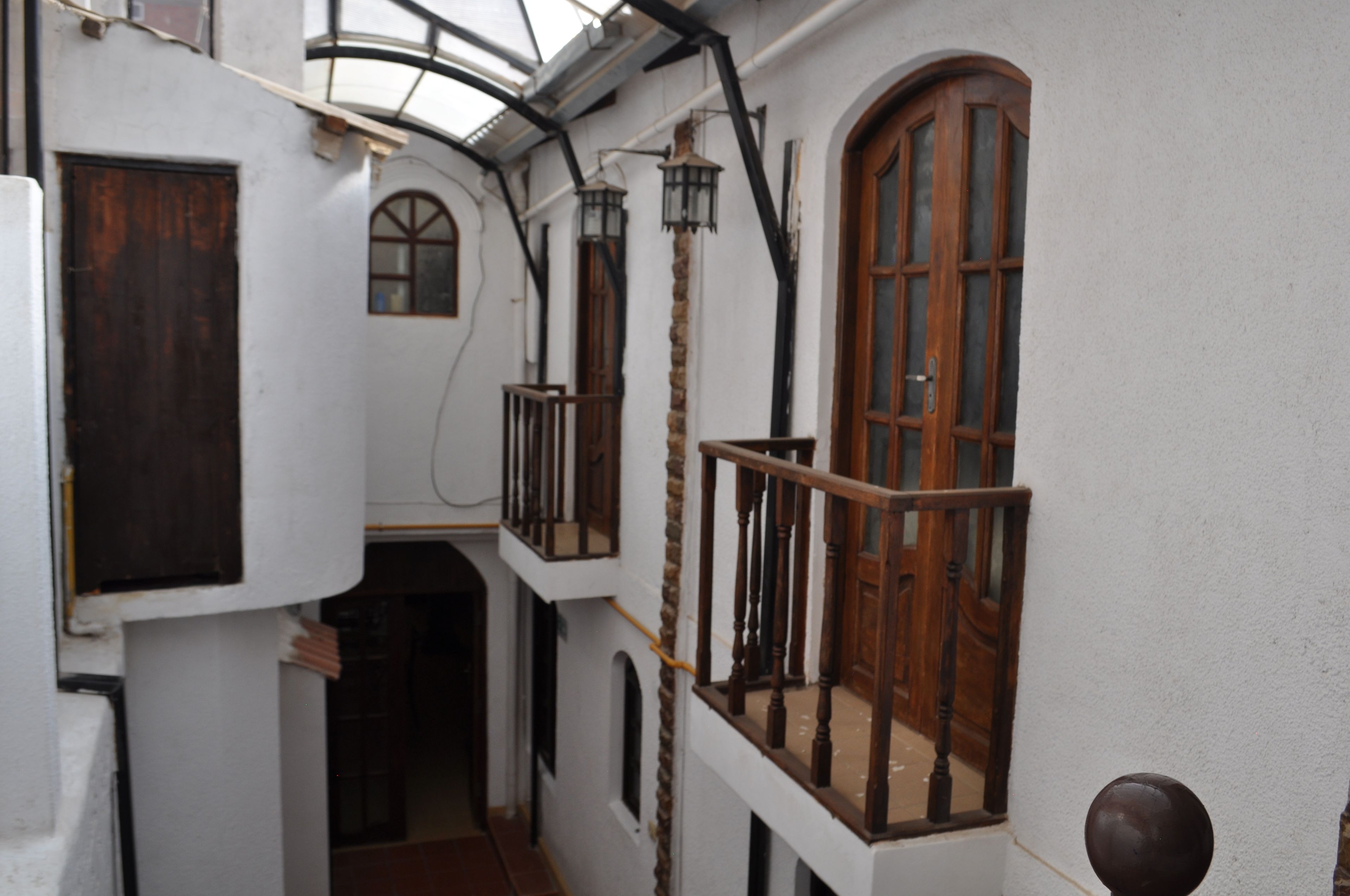 A narrow corridor with white walls, wooden doors, and a wooden balcony with a railing.