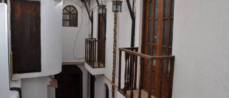 A narrow corridor with white walls, wooden doors, and a wooden balcony with a railing.