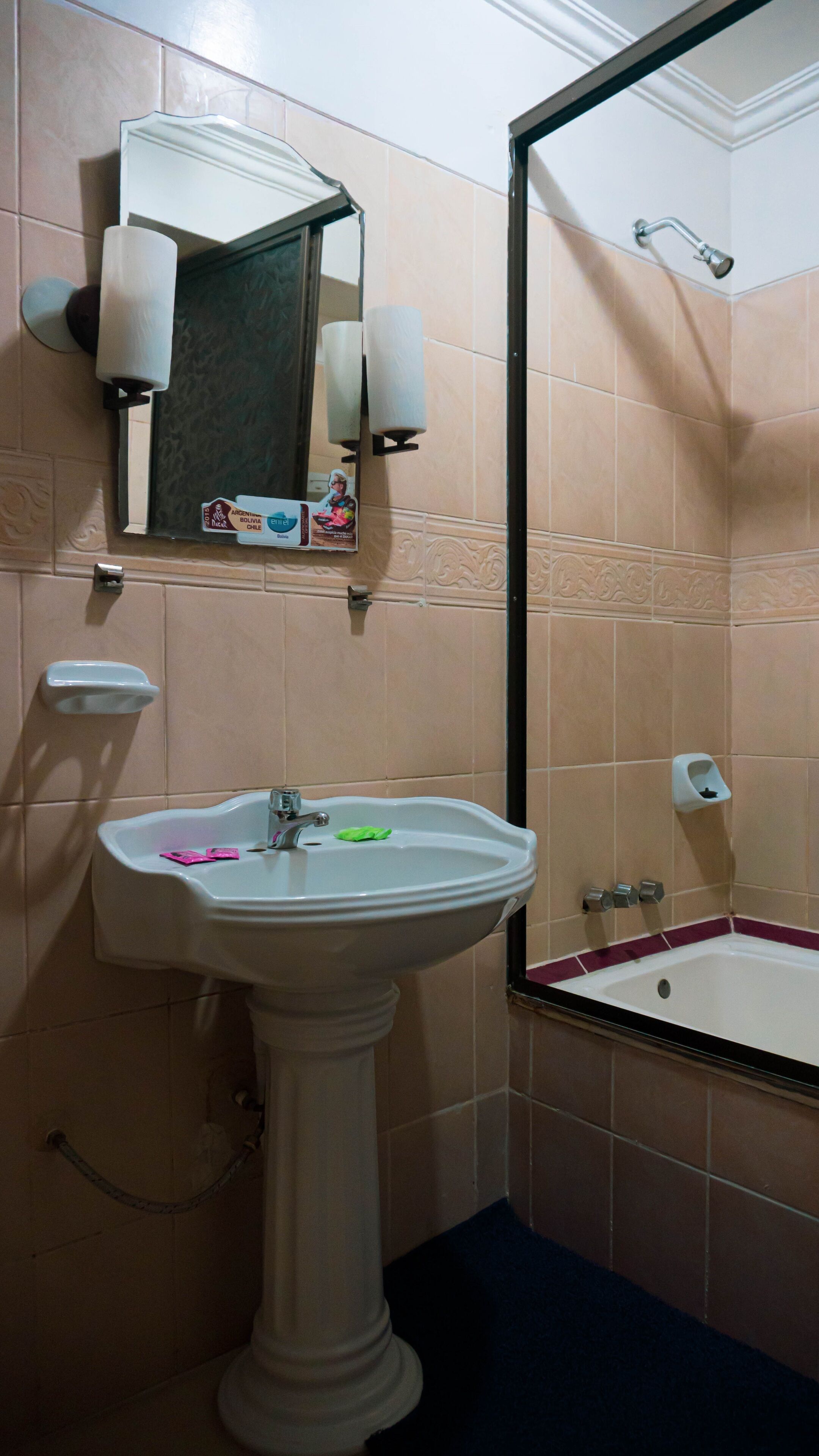 Un baño con lavamanos pedestal, espejo, secador de manos y zona de ducha.