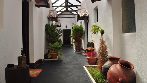 A narrow courtyard with potted plants, terracotta pots, and a black metal bell. - Hostal la Magia de Uyuni (Uyuni)