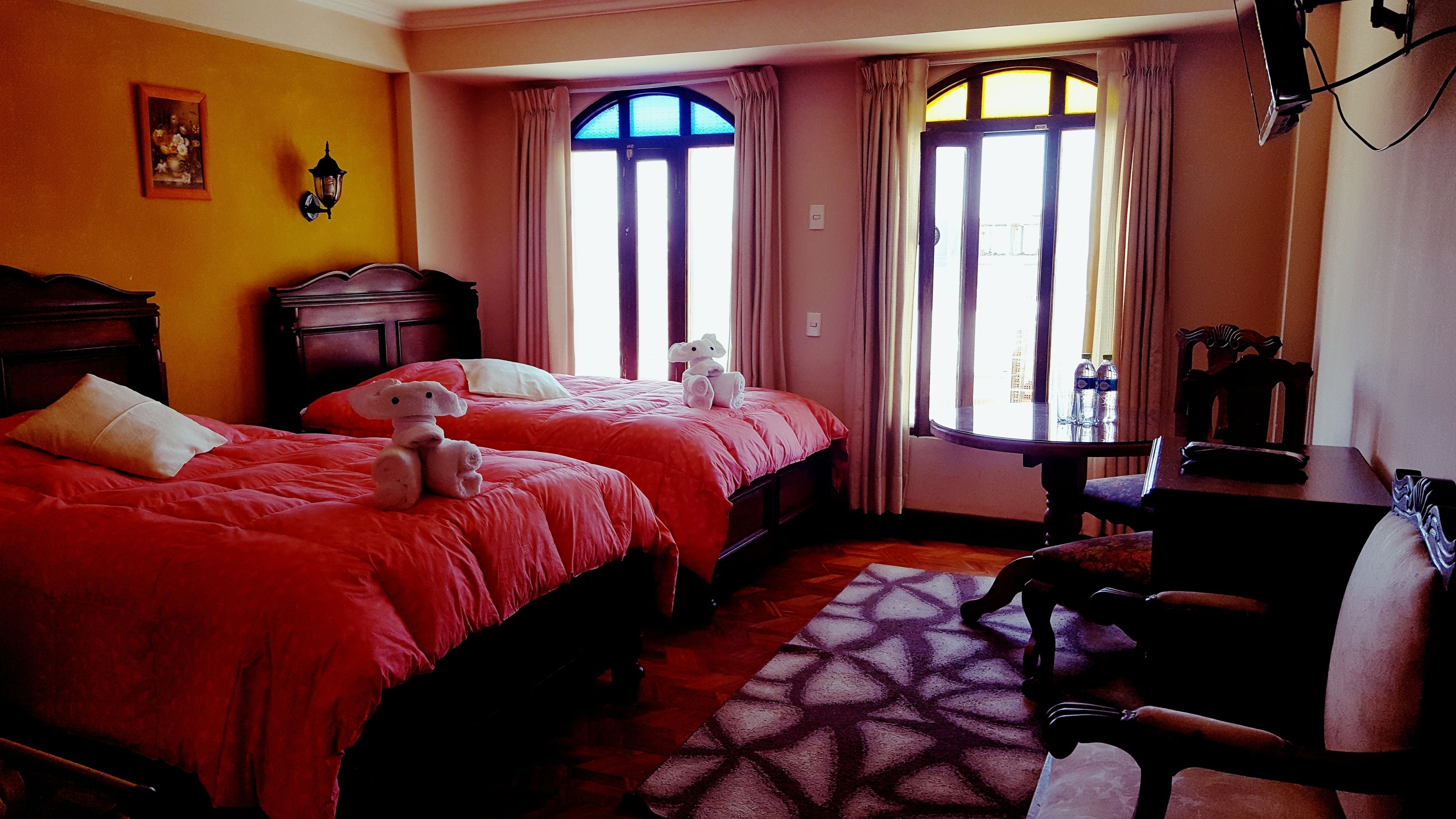 Una camera d'albergo con due letti, una scrivania in legno, una sedia e una finestra con tende.