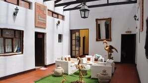 A courtyard with white walls, a tiled floor, and a seating area with white sofas and orange cushions. There are decorative bird sculptures and a large mirror on the wall. - Hostal la Magia de Uyuni (Uyuni)