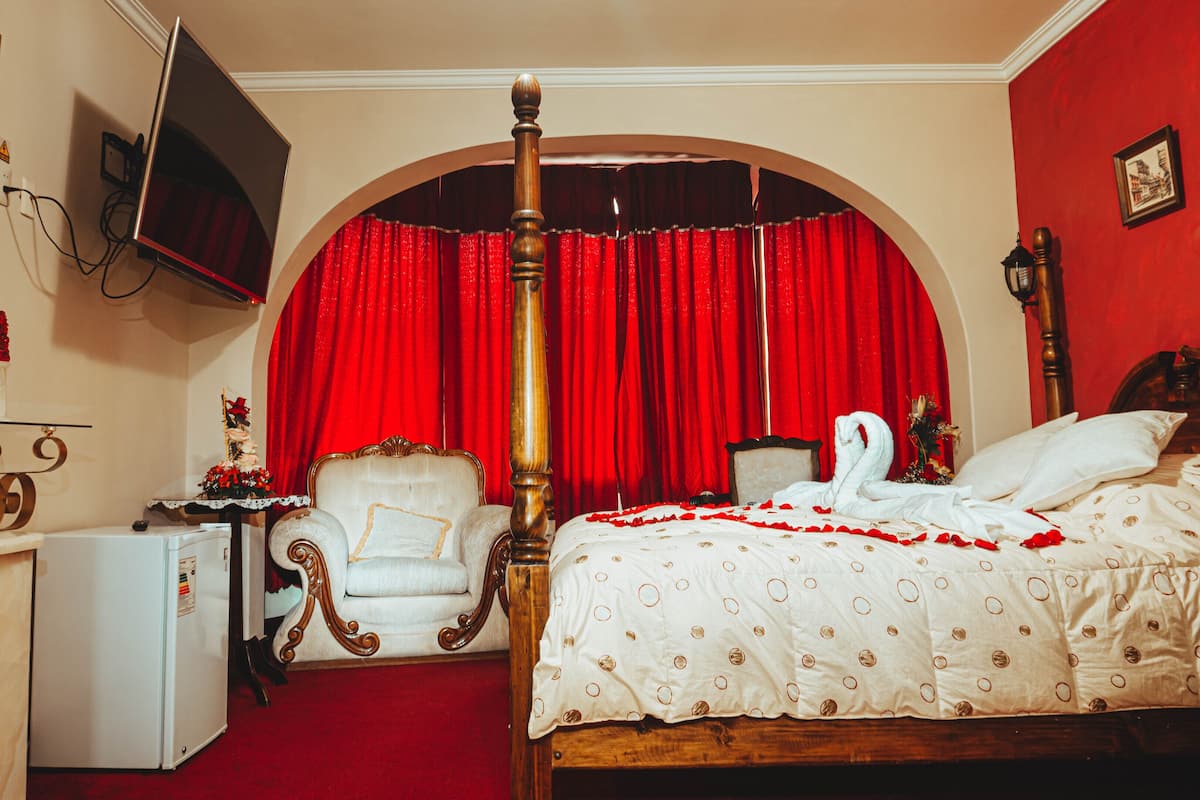Ein Himmelbett mit rotem Vorhang als Hintergrund, ein Fernseher und ein kleiner Kühlschrank.