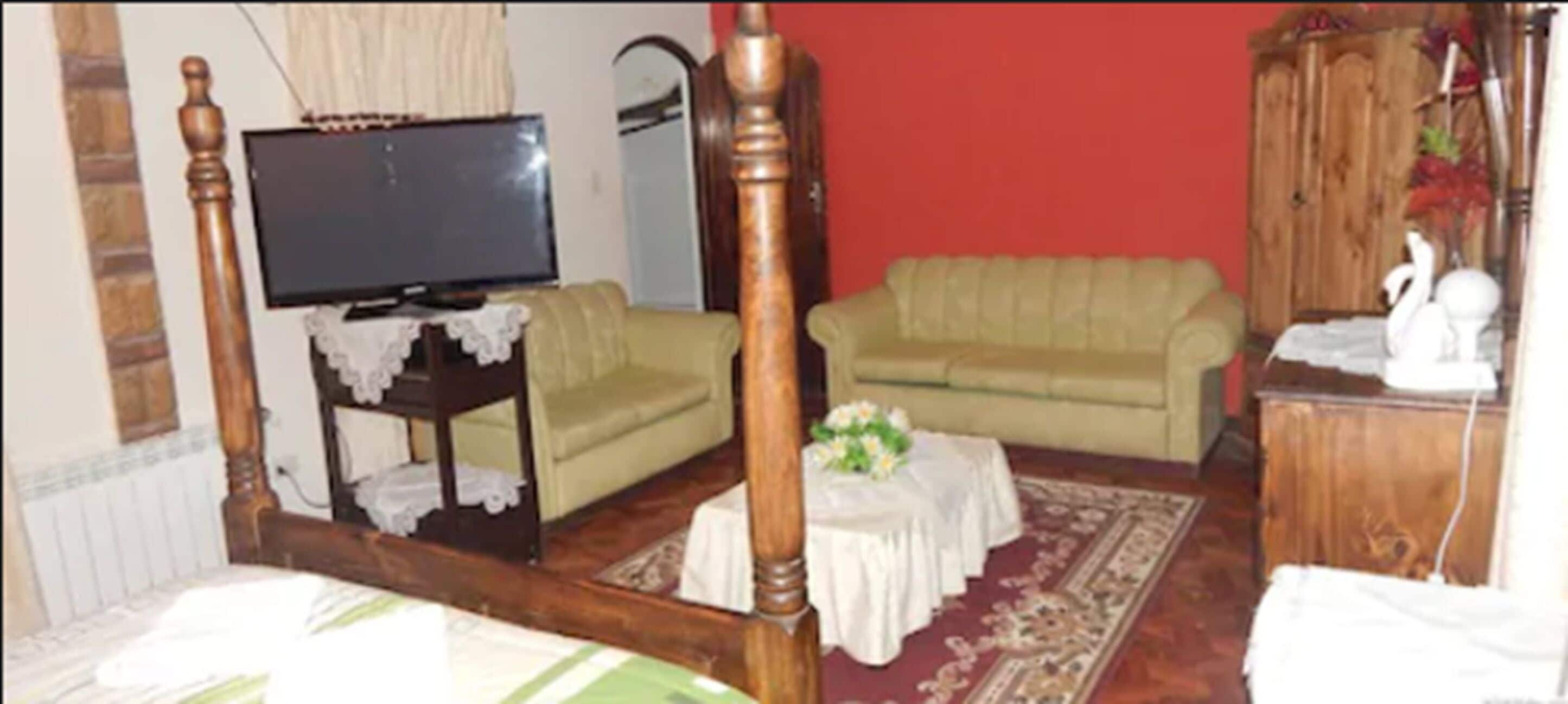 Une chambre à coucher avec un lit à baldaquin, un téléviseur posé sur un meuble en bois, un canapé vert et une armoire en bois.