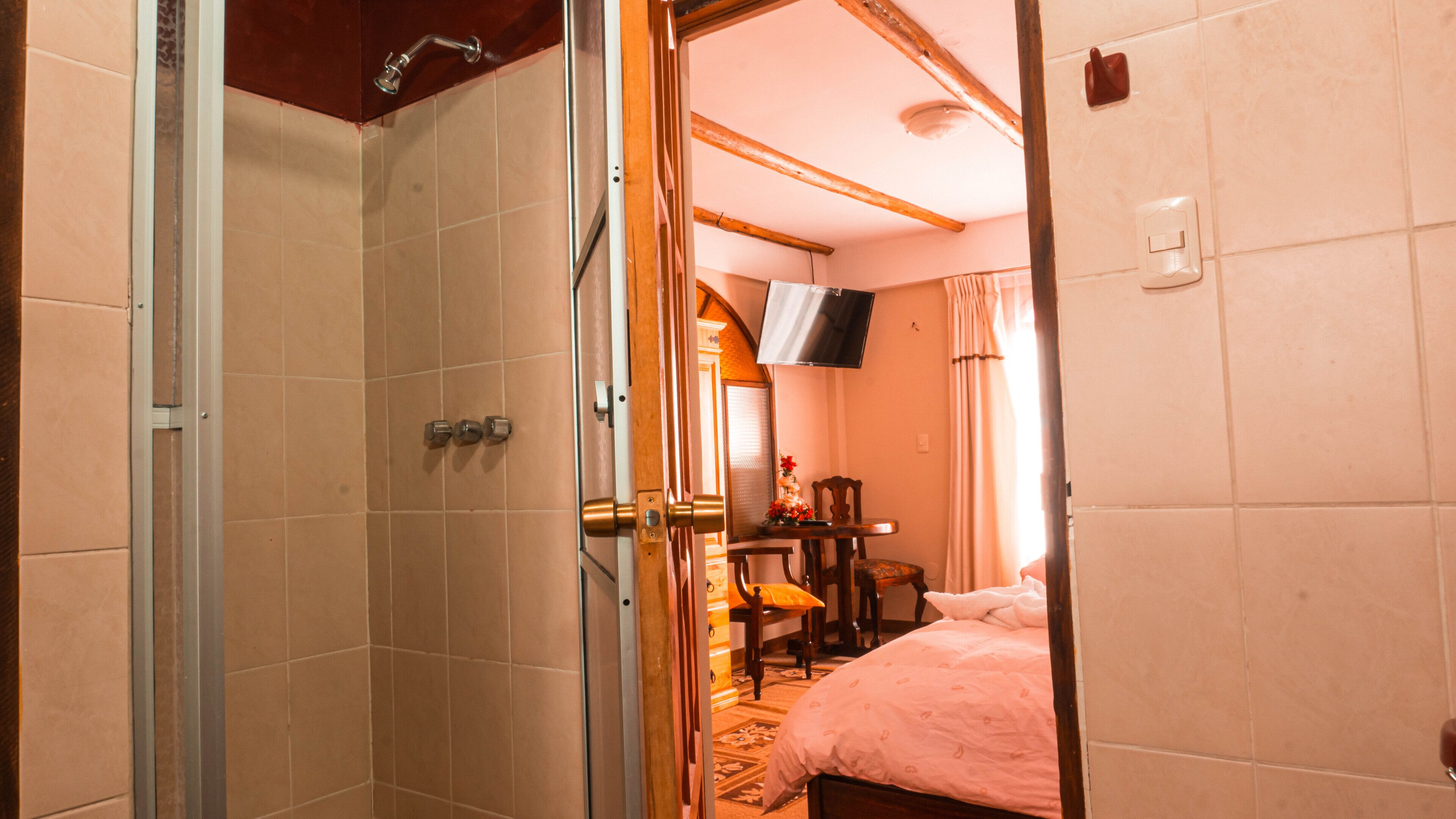 Une chambre avec une douche, un lit, une table avec des chaises et un téléviseur fixé au mur.