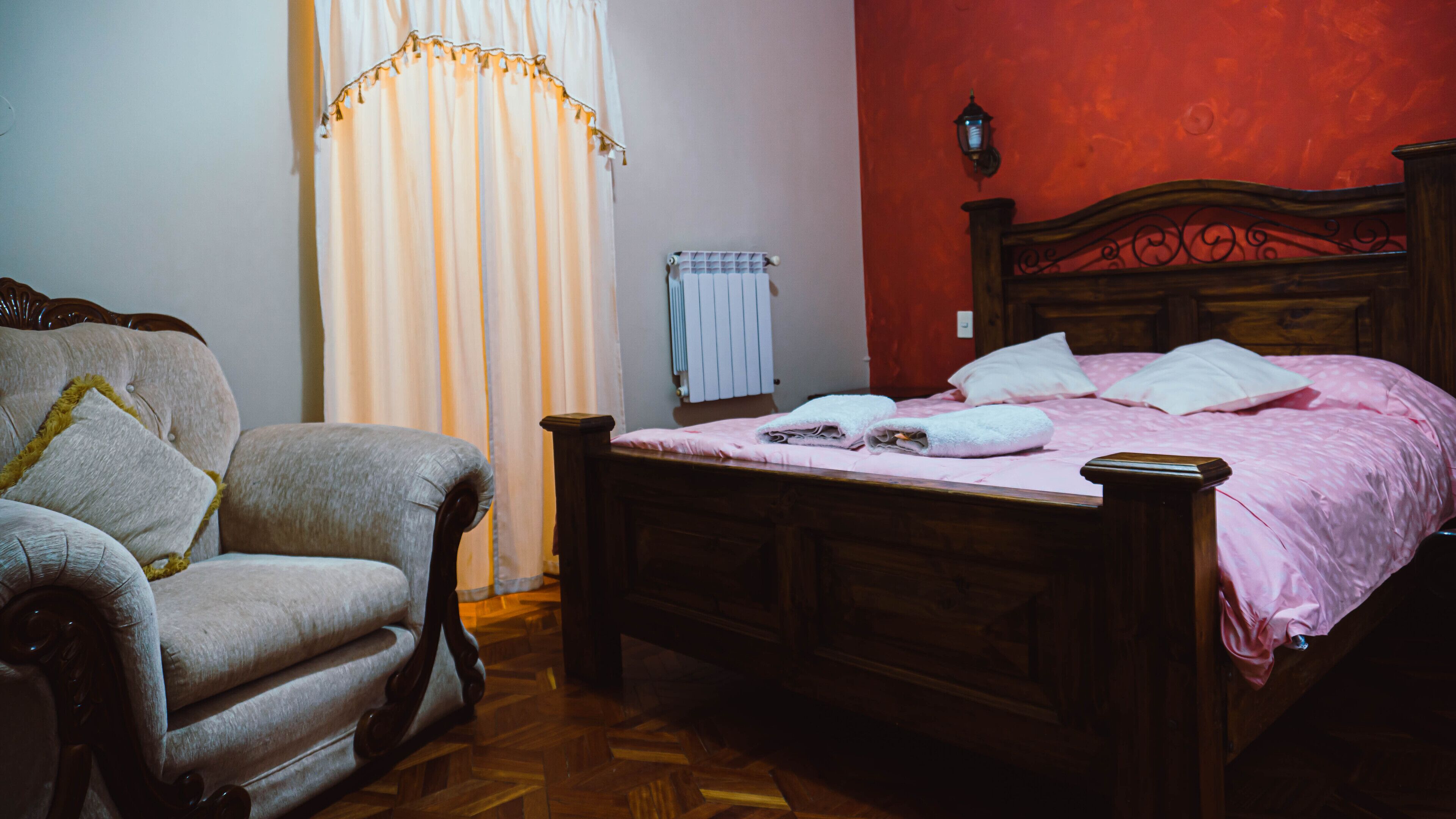 Un dormitorio con una cama de madera, una silla, un radiador y una ventana con cortinas.