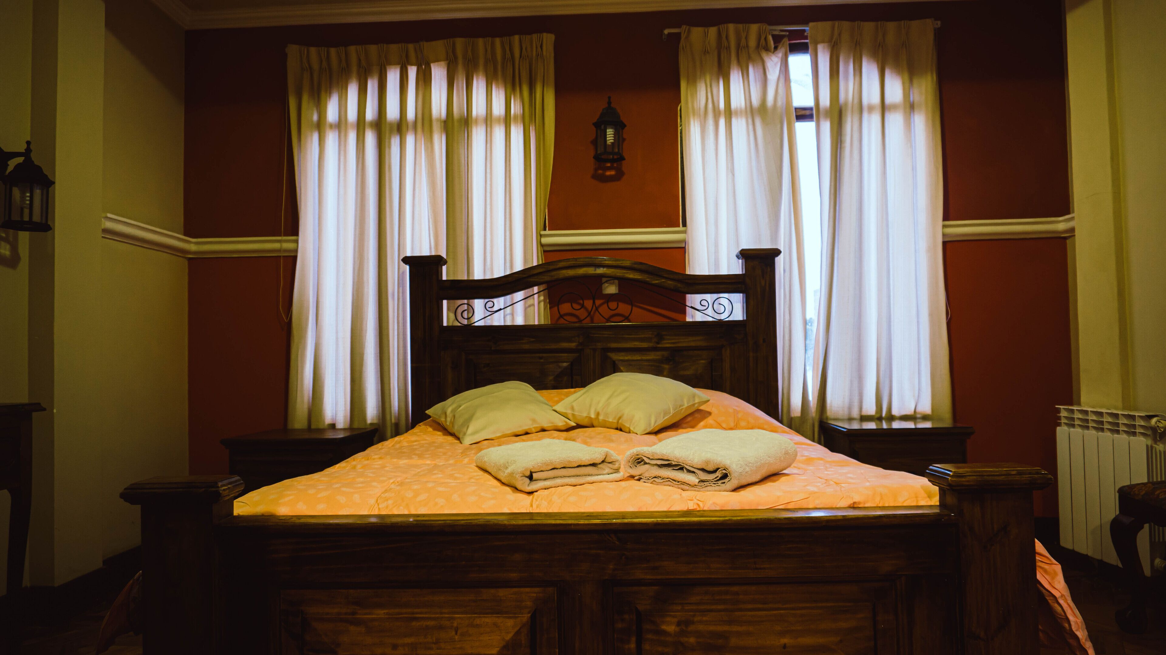 A wooden bed with a headboard, two nightstands, and a window with curtains.