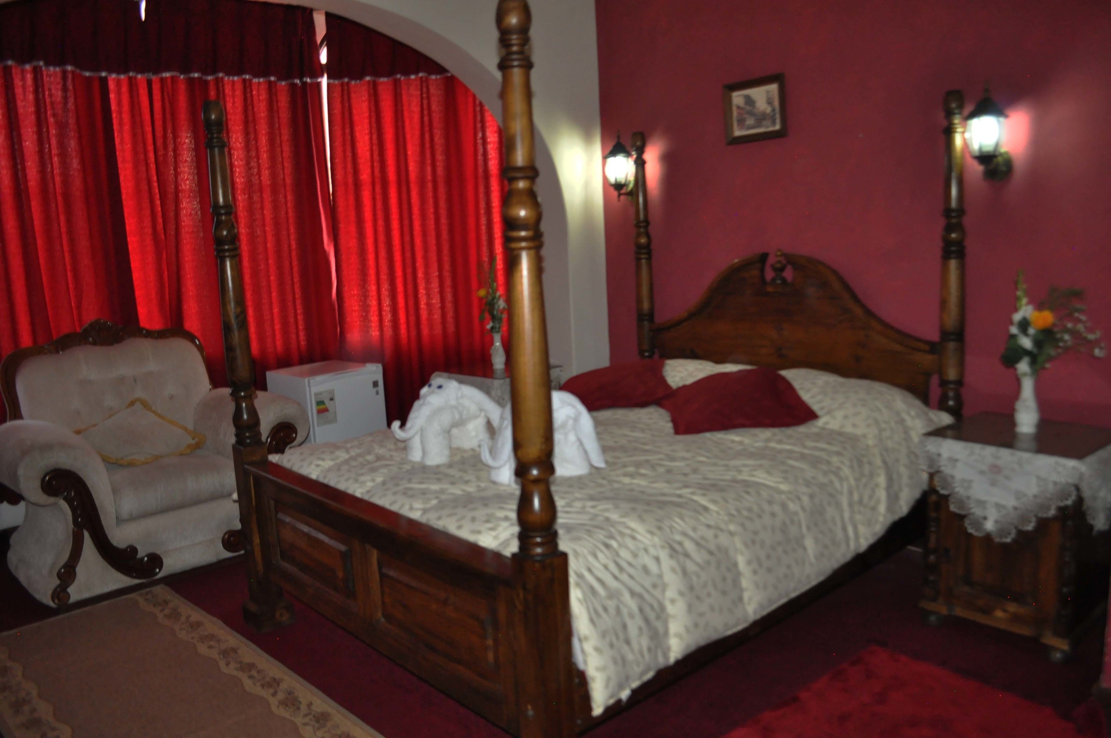 A bedroom with a four-poster bed, a wooden chair, a nightstand, and a red curtain.