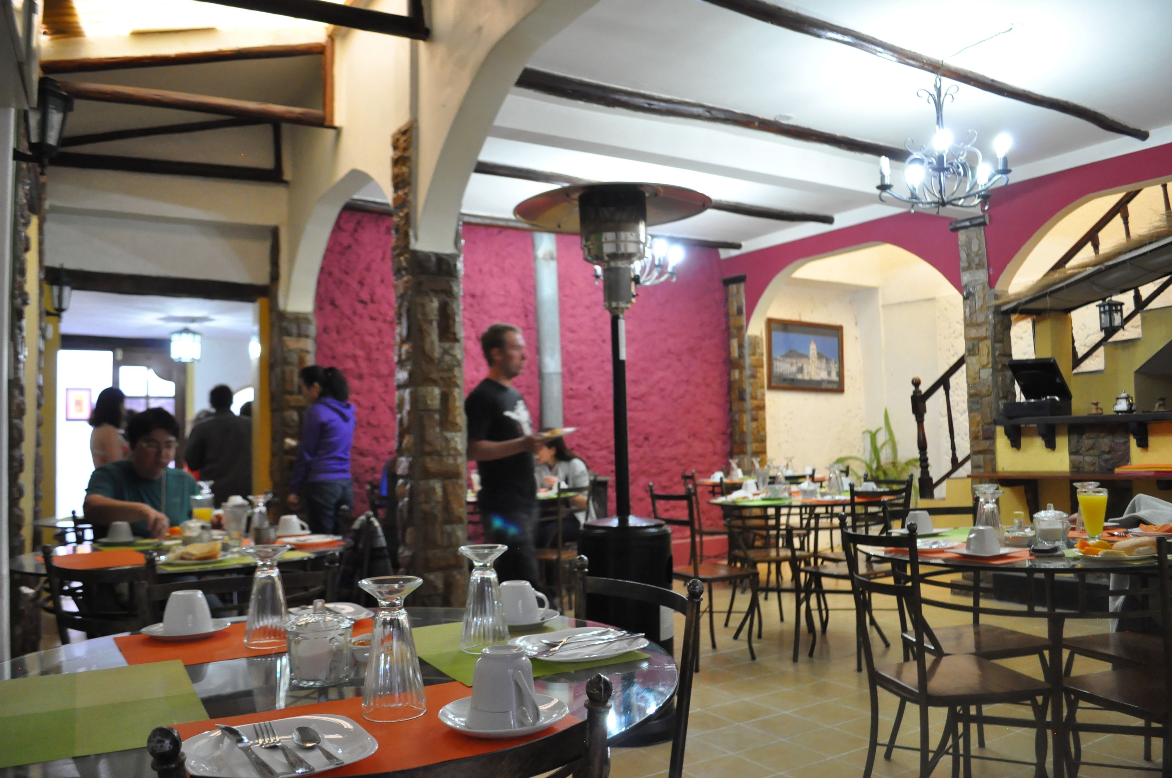 A restaurant with tables set for dining, a waiter attending to guests, and a distinctive pink wall.