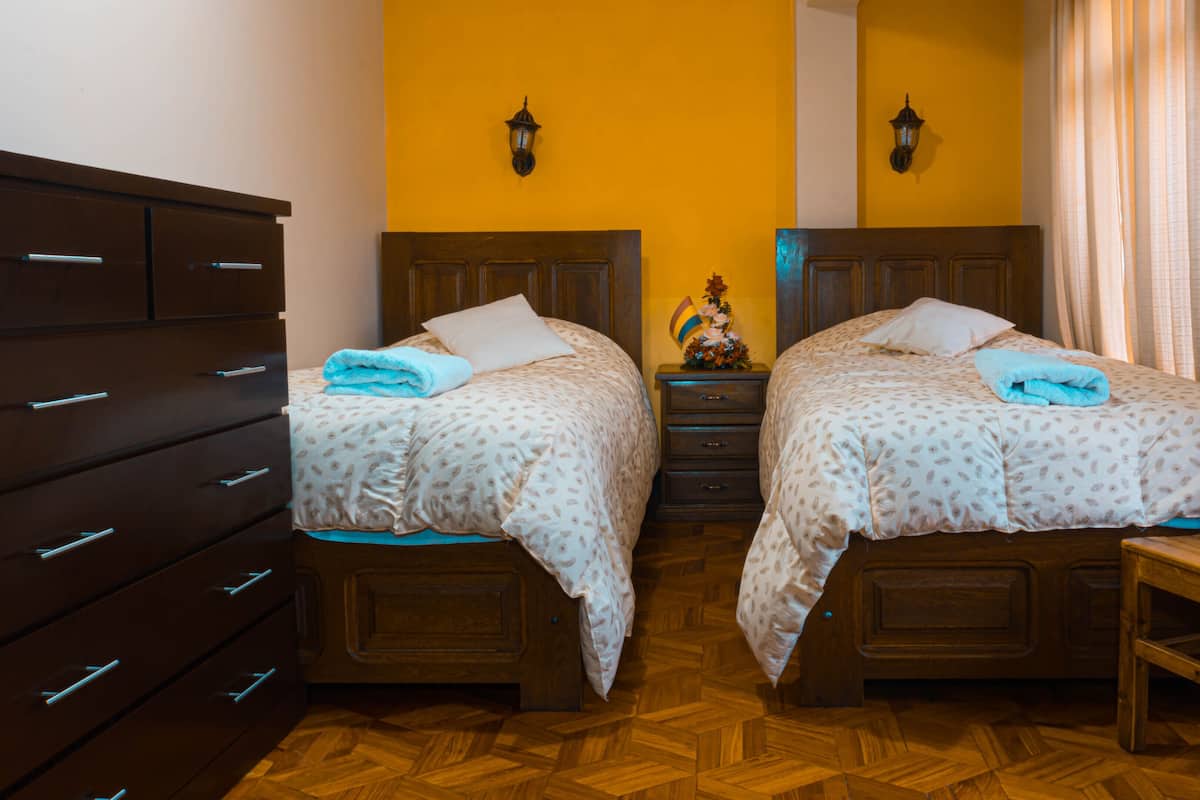 Ein Zimmer mit zwei hölzernen Betten, einem Holzstuhl, einem Schmuckkästchen und einem kleinen Tisch mit einer Dekoration.
