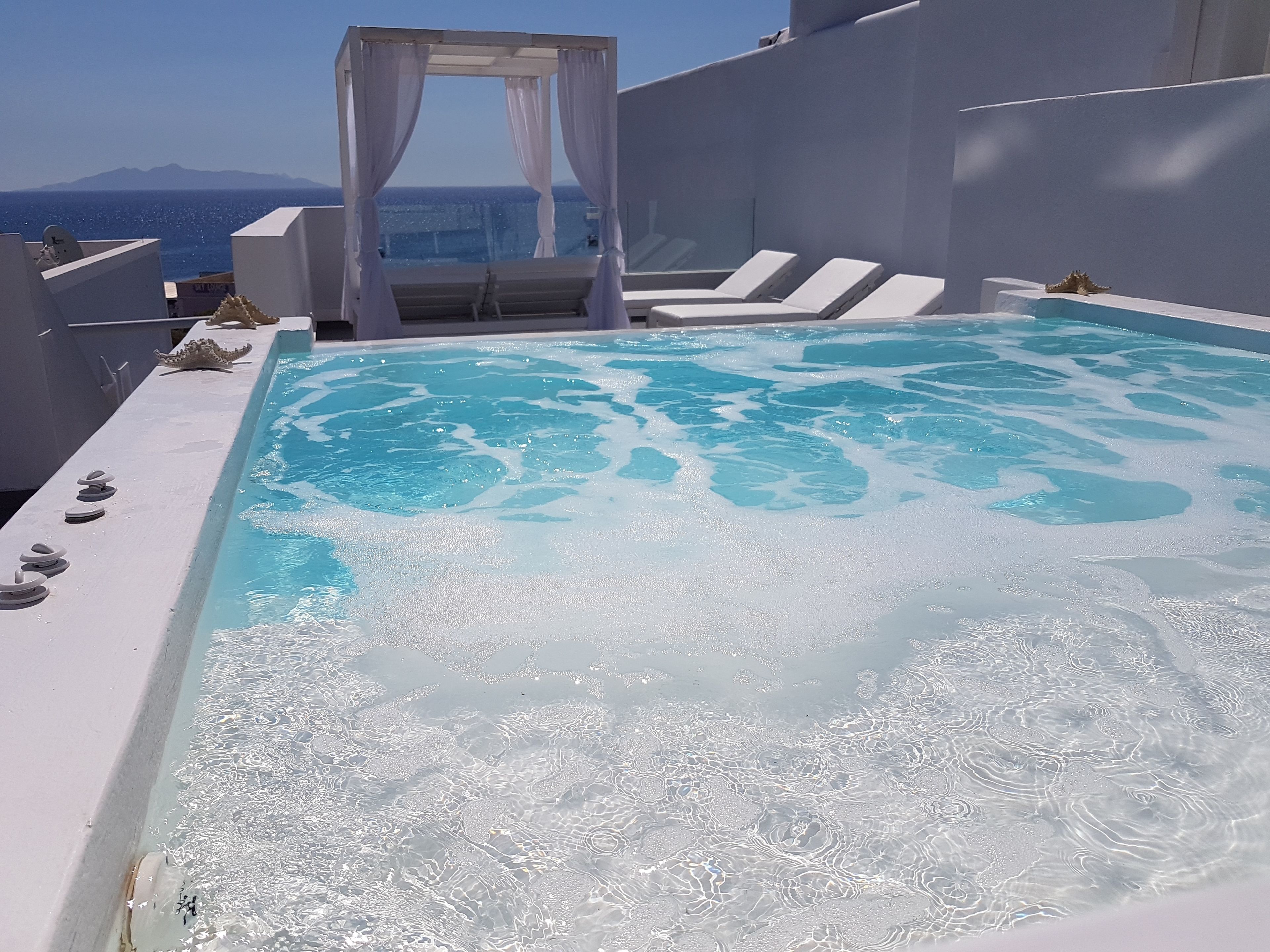 Une piscine à débordement située sur le toit, avec une eau d’un bleu cristallin, des chaises longues blanches et une vue imprenable sur la mer et les montagnes.