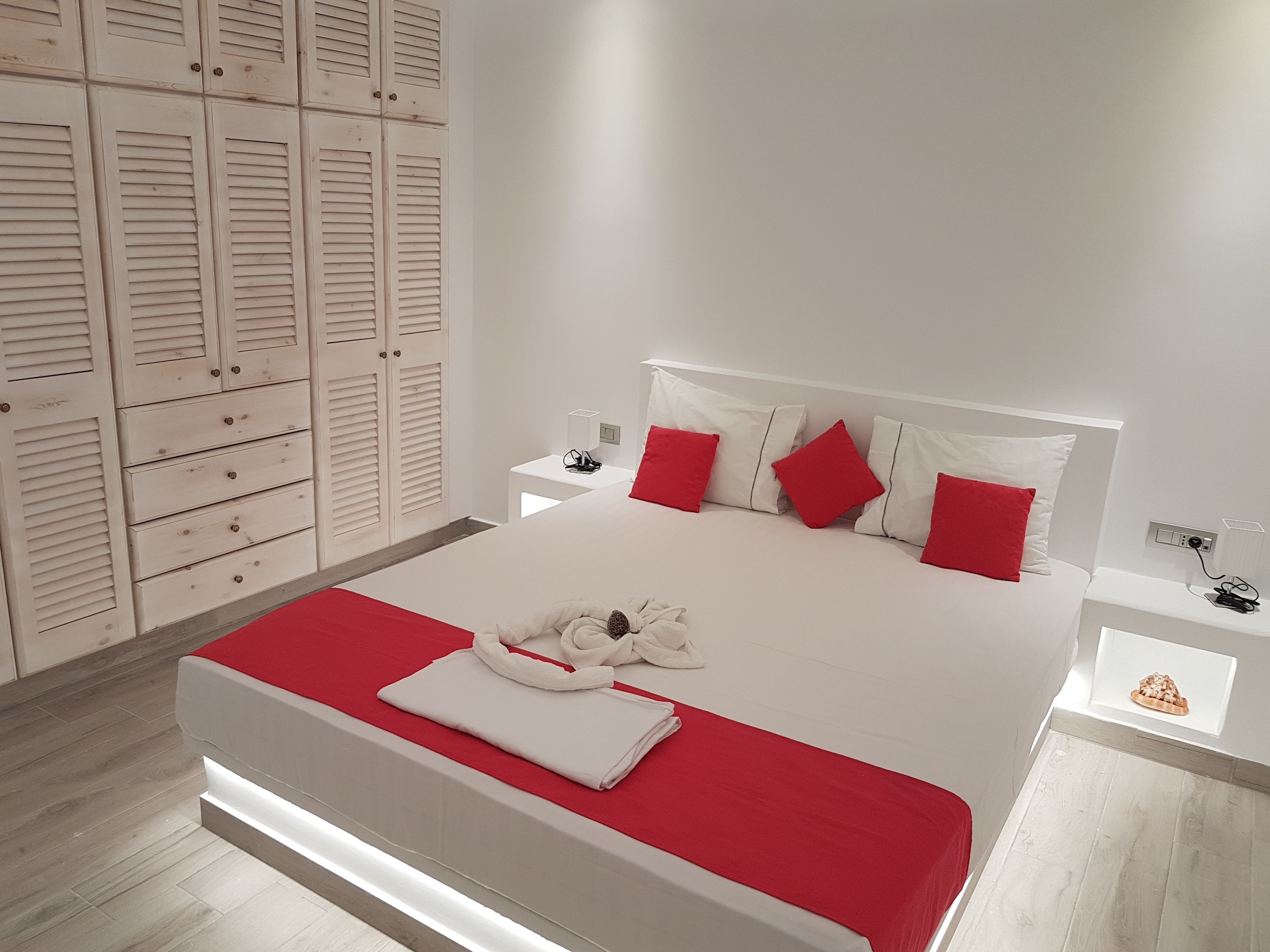 A neatly arranged bedroom with a large bed, white walls, and a wooden wardrobe.