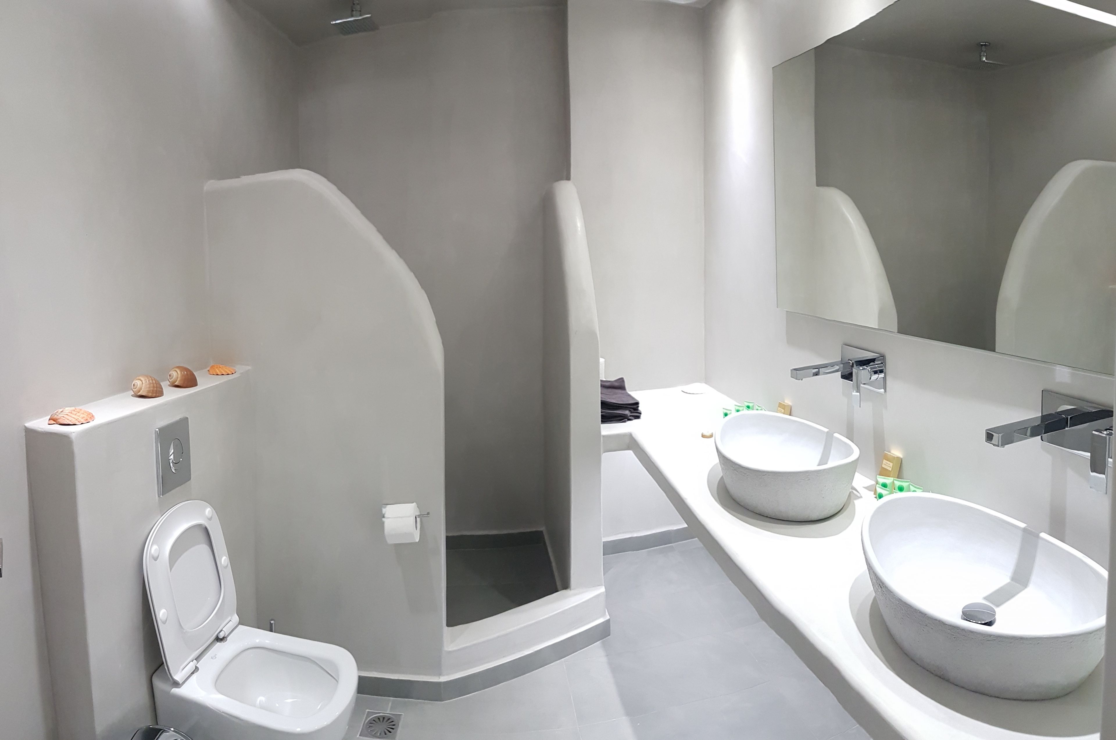 A modern bathroom with a toilet, a shower, and a sink with a large mirror.