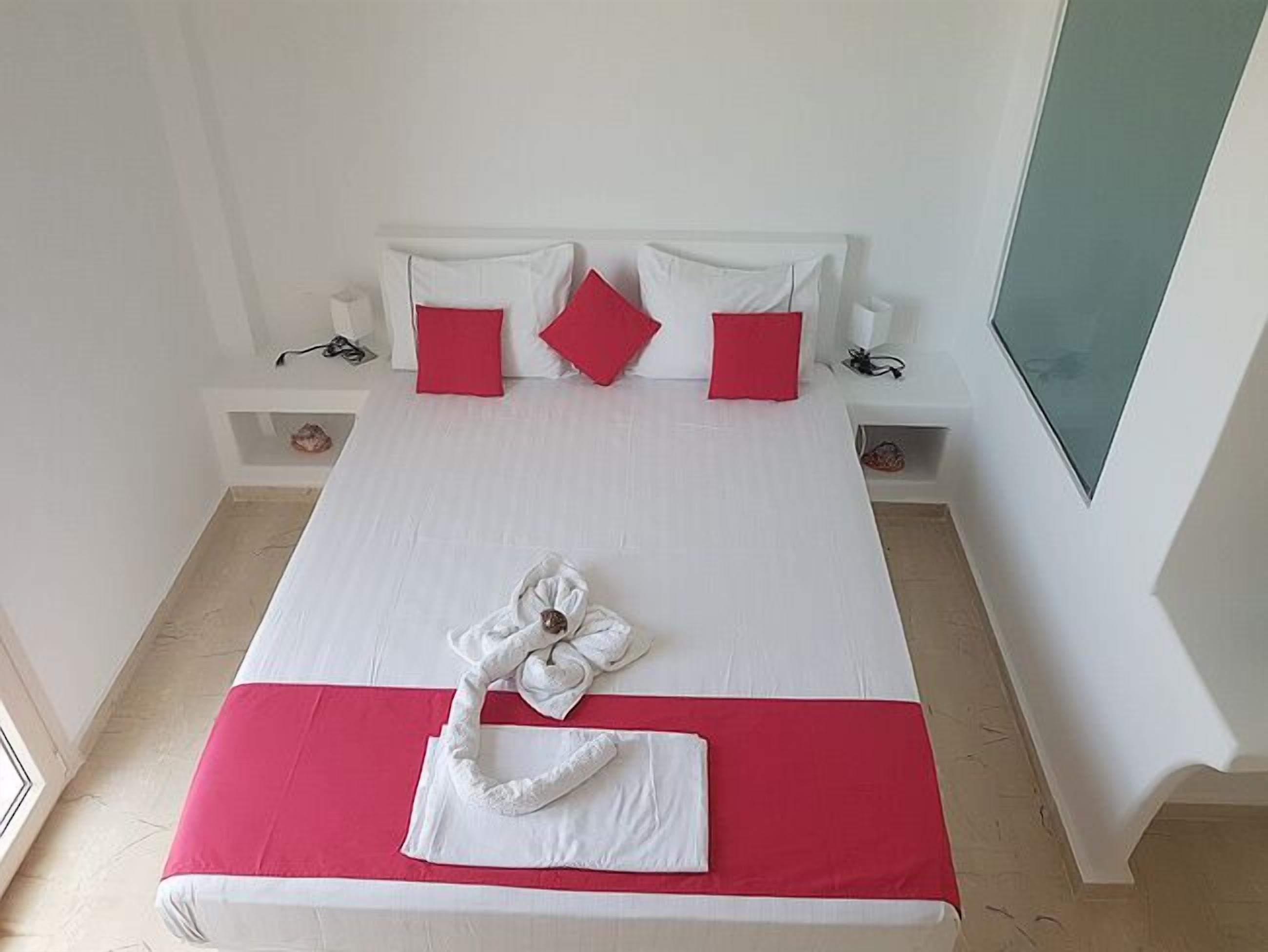A neatly made bed with white and red bedding, a heart-shaped towel, and two red pillows.