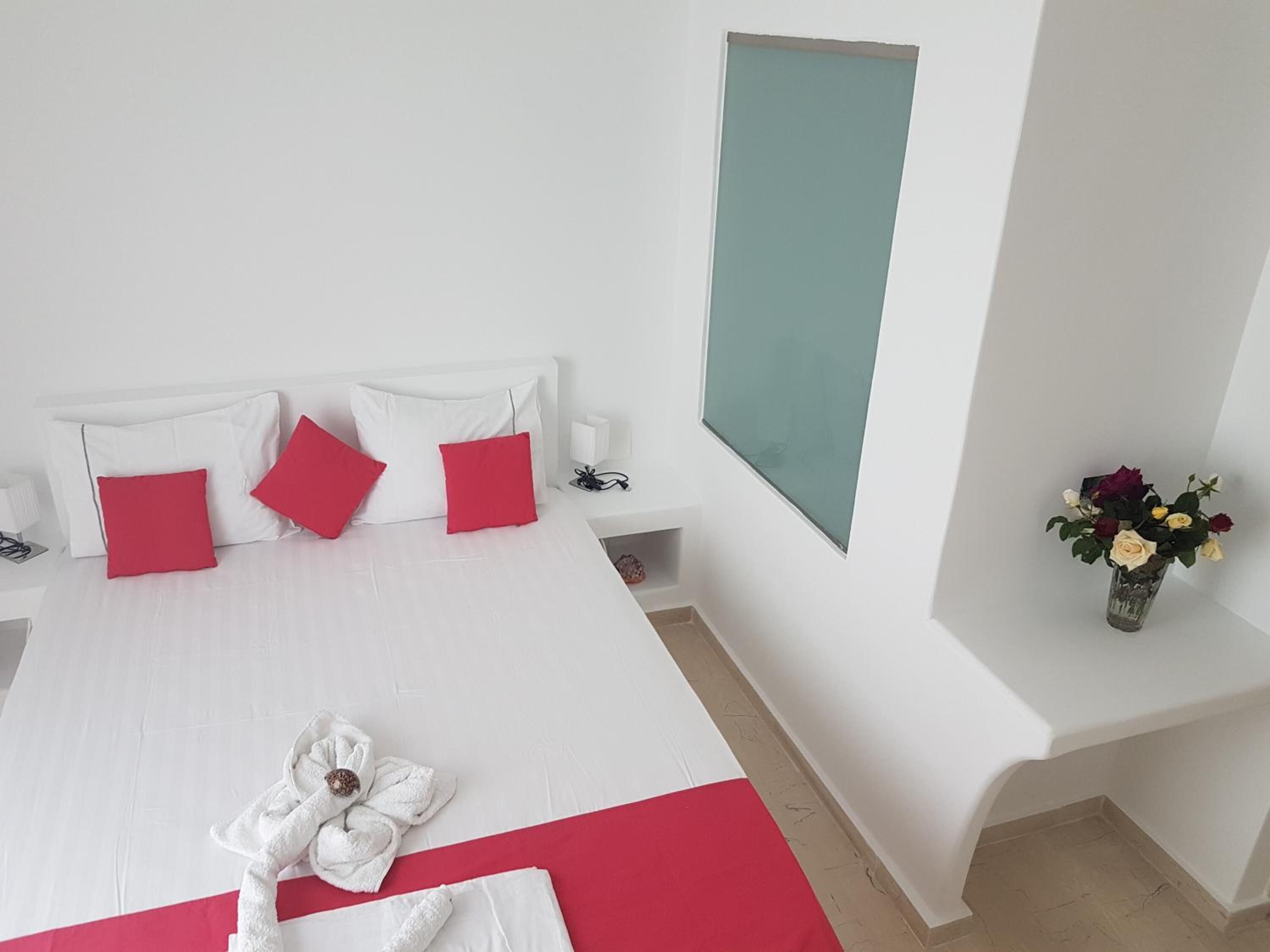 A hotel room with a large bed, white walls, a teal accent wall, and a vase with flowers on a nightstand.