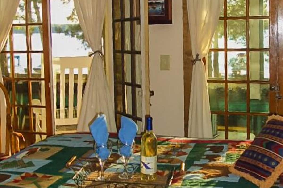 A room with a large window, a table with a bottle and glasses, and a patterned tablecloth.
