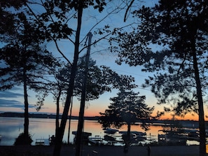 A lakeside view with trees, a dock, and boats. - Lake Ripley Lodge w Lake Front Rooms, Grand Porch, Kayaks & Paddleboard (Cambridge)