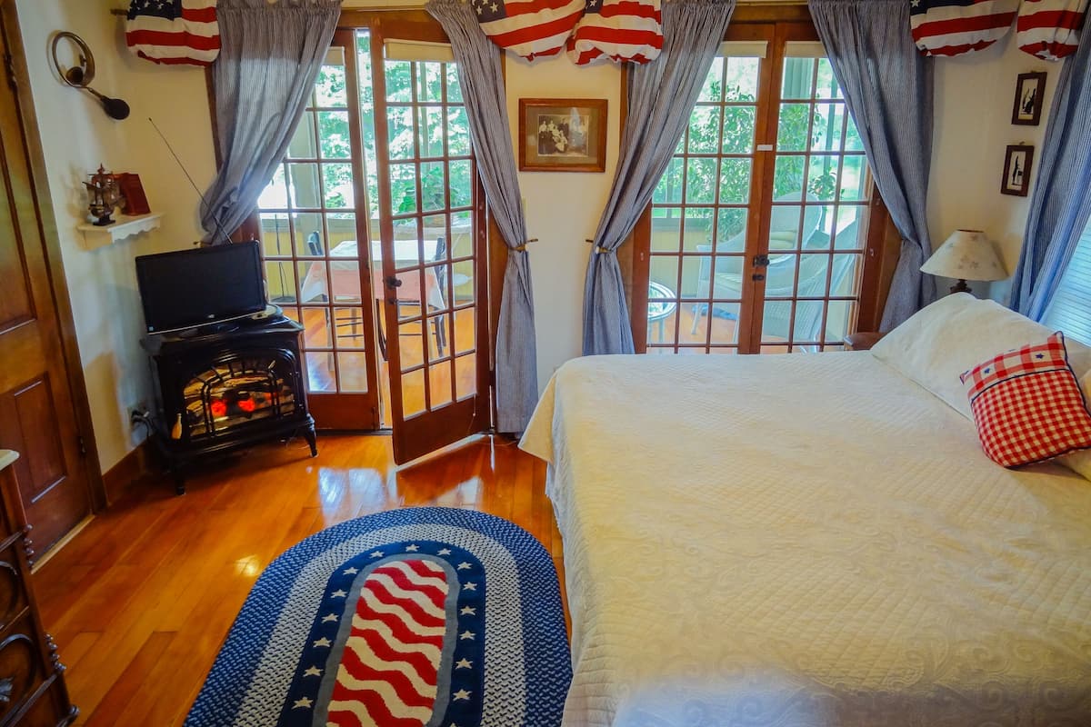 A bedroom with a bed, a television, a fireplace, and a view of the outdoors through a door.