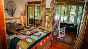 A bedroom with a large bed, a rocking chair, and a view of the outdoors through a glass door. - Lake Ripley Lodge w Lake Front Rooms, Grand Porch, Kayaks & Paddleboard (Cambridge)