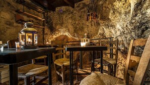 Um interior rústico com mesas e cadeiras de madeira, paredes de pedra e lanternas penduradas.