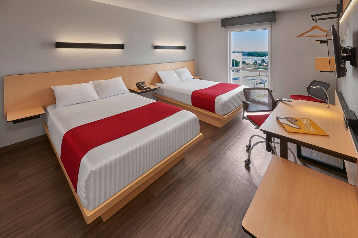 Une chambre d’hôtel avec deux lits, un bureau, une chaise, une télévision et une fenêtre donnant sur un beau paysage.