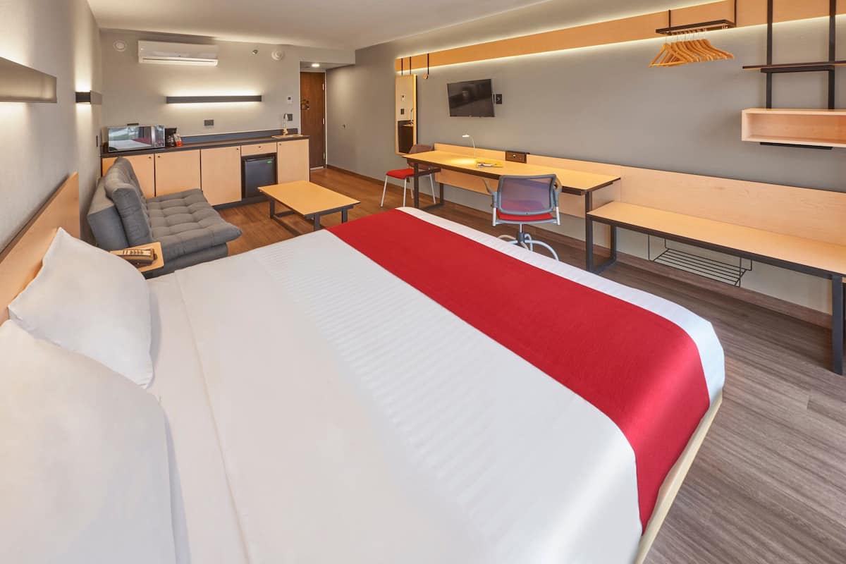 Une chambre d’hôtel avec un grand lit, un bureau, une chaise, un canapé et une kitchenette.