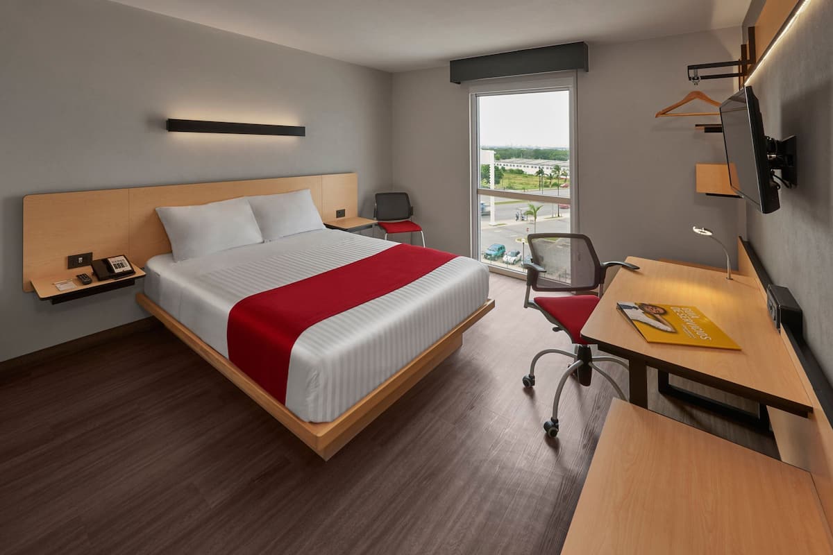 Une chambre d’hôtel avec un lit, un bureau, une chaise et une fenêtre donnant sur un paysage agréable.