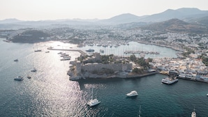 An aerial view of a coastal city with a prominent castle-like structure surrounded by water, boats, and a marina. - Artemis Hotel (Bodrum)