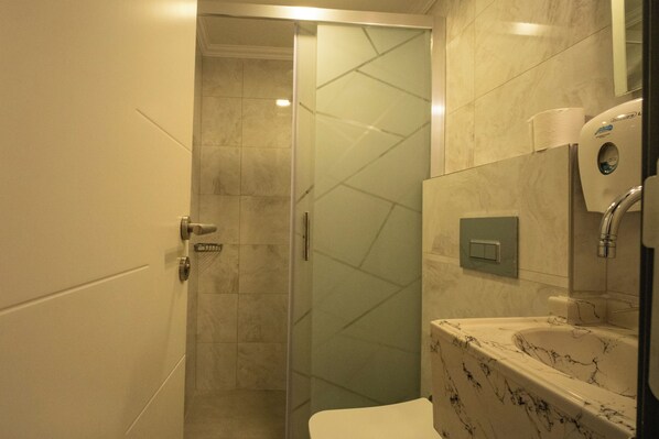 A bathroom with a glass shower door, a marble sink, and a toilet.