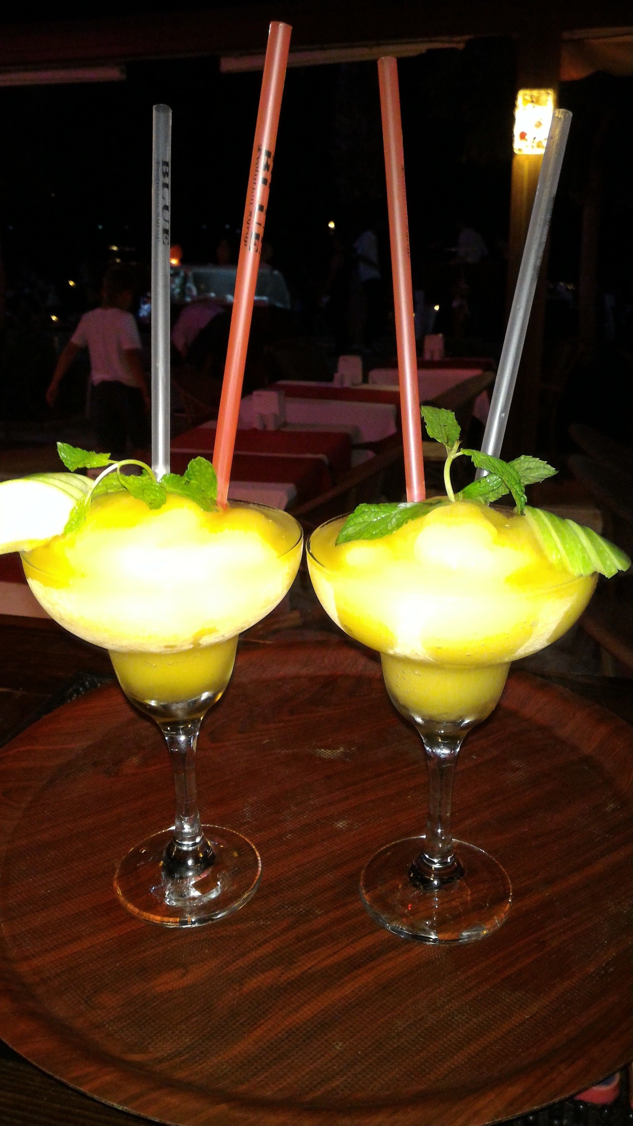 Two cocktails with straws and mint leaves on a wooden table.