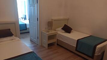A small, simple room with two single beds, a nightstand, and a desk.