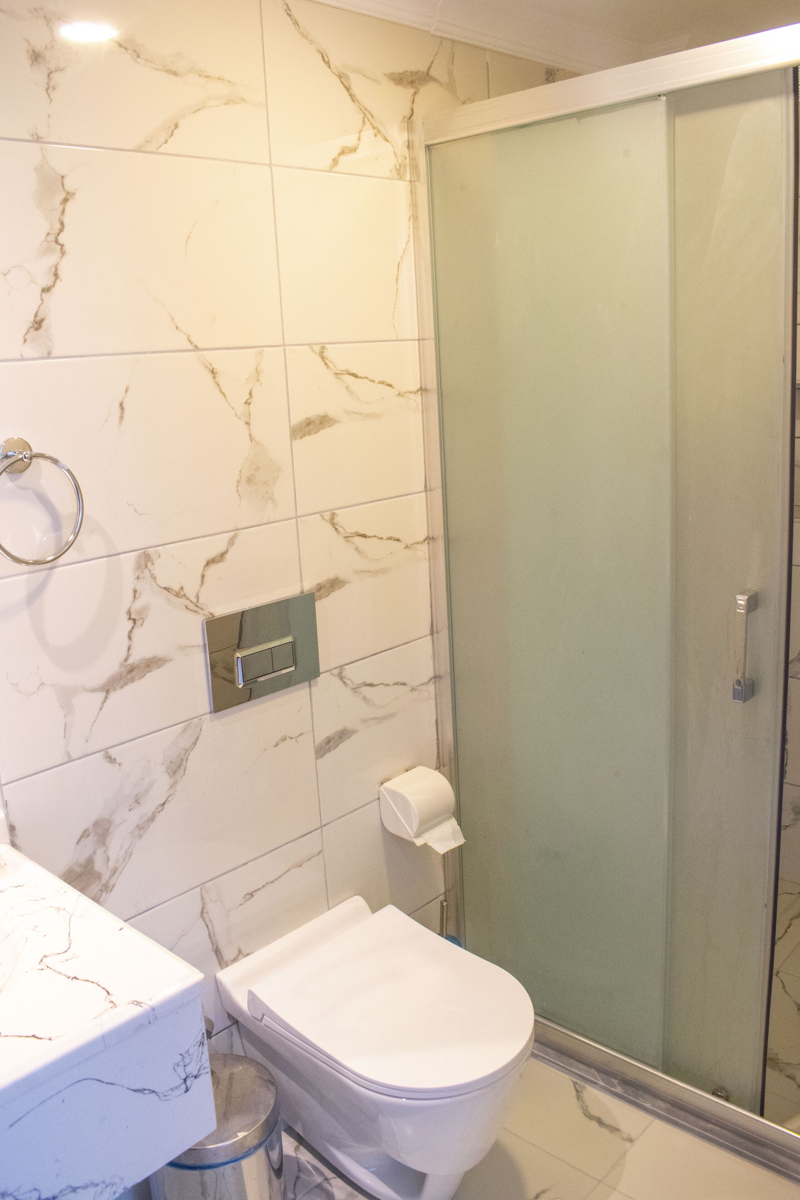 A bathroom with a toilet, a glass shower enclosure, and marble tiles.