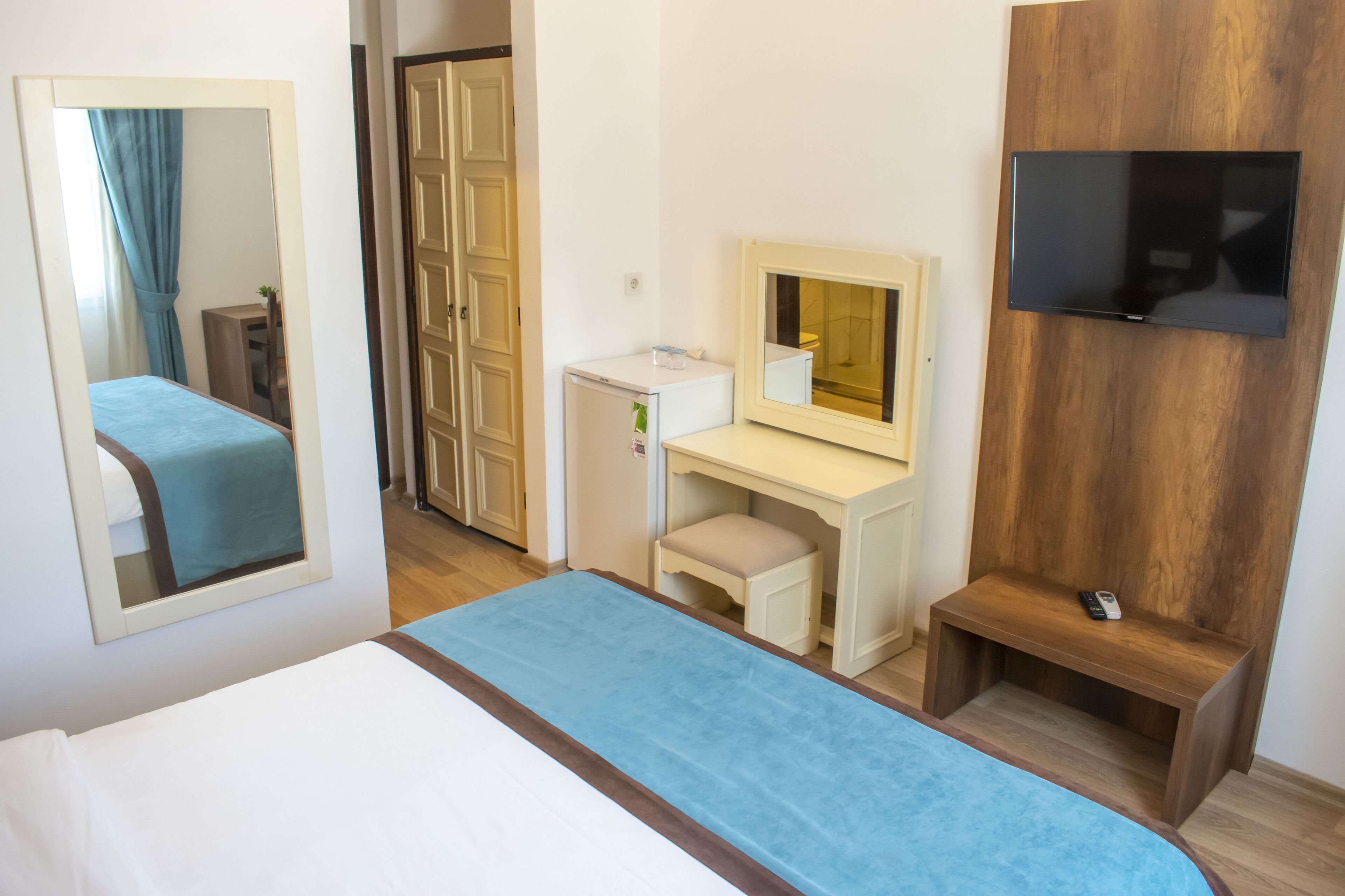 Une chambre d’hôtel comprenant un lit, un bureau avec un miroir, une télévision et un petit tabouret.