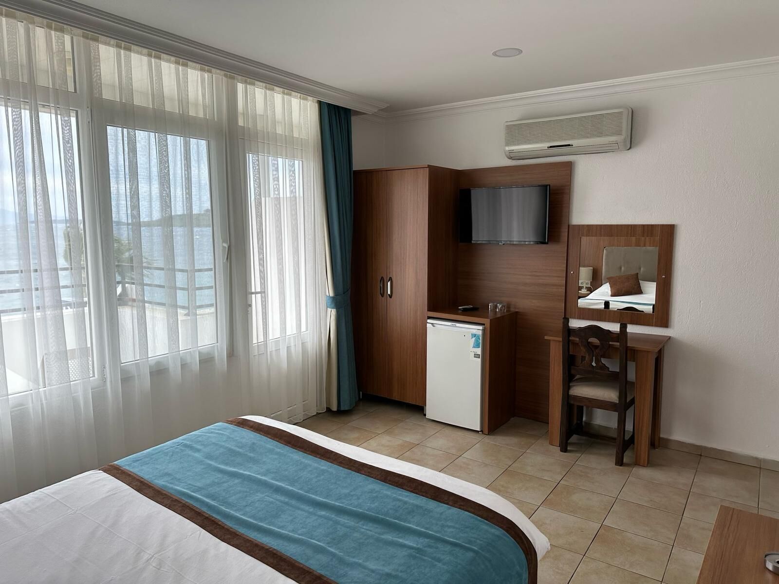 A hotel room with a bed, a desk, a chair, a television, and a minibar.