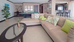 Una sala moderna con un sofá color beige, una mesa de billar y una mesa de centro de vidrio.