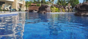 A swimming pool with clear blue water, surrounded by lounge chairs and a bridge.