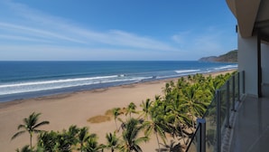 Vista de la playa desde un balcón, con palmeras y olas del océano.