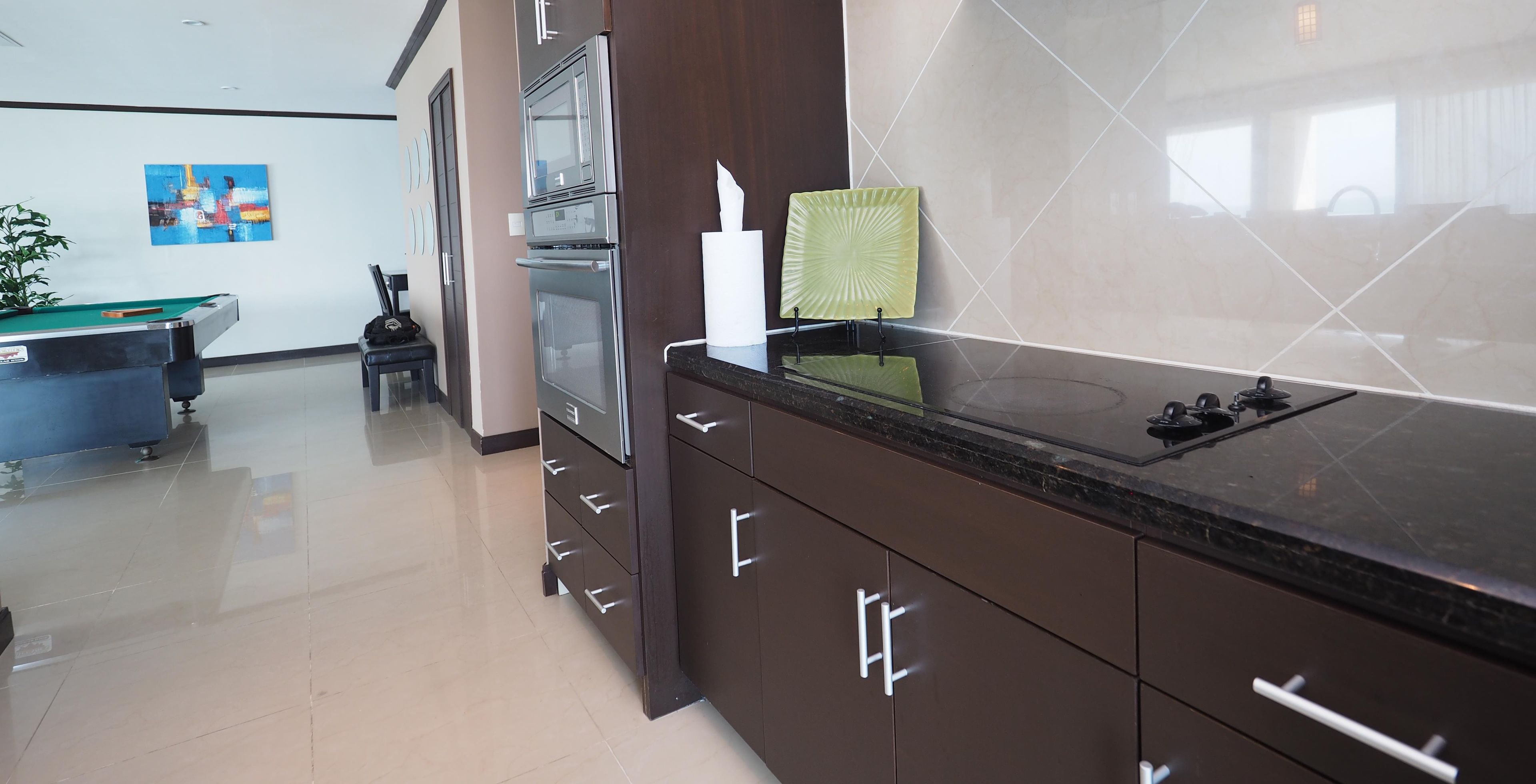 A modern kitchen with dark cabinetry, a stainless steel refrigerator, and a black countertop.