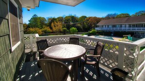 A covered outdoor deck with a round table and chairs, a white fence, and a view of trees and a building. - Harborside Motel (Montauk)