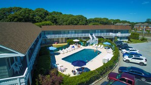 A hotel with a swimming pool surrounded by lounge chairs and umbrellas, a covered deck, and a parking lot with cars. - Harborside Motel (Montauk)