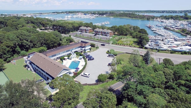 An aerial view of a marina with boats, a swimming pool, and a building with a parking lot. - Harborside Motel (Montauk)