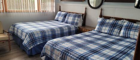 A room with two beds, each with a blue and white checkered bedspread, a wooden headboard, a bedside table, and a mirror on the wall.