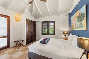 A hotel room with a bed, a window with shutters, a wall-mounted lamp, and a painting. - Blue Bay Villas (Sint Michiel)