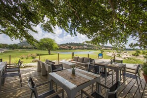 An outdoor deck with wooden furniture, a view of a golf course, and a lake in the background. - Blue Bay Villas (Sint Michiel)
